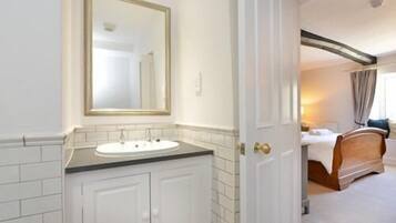 Un baño de hotel con un tocador blanco, un espejo y una puerta que da a un dormitorio.
