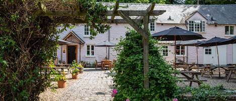 A courtyard with a wooden pergola, outdoor seating, and a building with multiple windows.