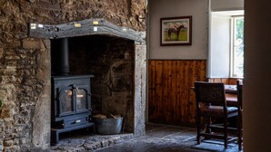 Una chimenea de piedra rústica con estufa de leña, un sillón de madera y un cuadro en la pared.