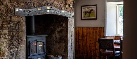 A rustic stone fireplace with a wood-burning stove, a wooden chair, and a framed picture on the wall.
