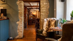 Un interior rústico con un arco de piedra que da a un comedor, suelo de madera y mobiliario de cuero.
