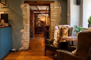 A rustic interior with a stone archway leading to a dining area, wooden flooring, and leather furniture.