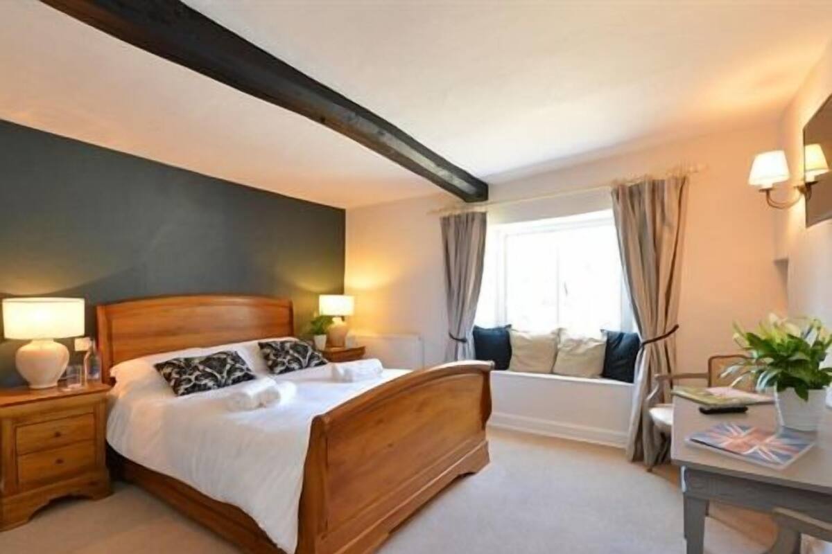 A bedroom with a wooden bed, bedside tables with lamps, a window with curtains, and a view of a bathtub.