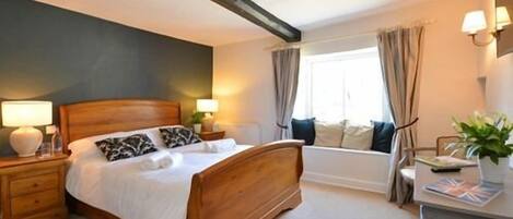 A bedroom with a wooden bed, bedside tables with lamps, a window with curtains, and a view of a bathtub.