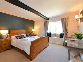 A bedroom with a wooden bed, bedside tables with lamps, a window with curtains, and a view of a bathtub.