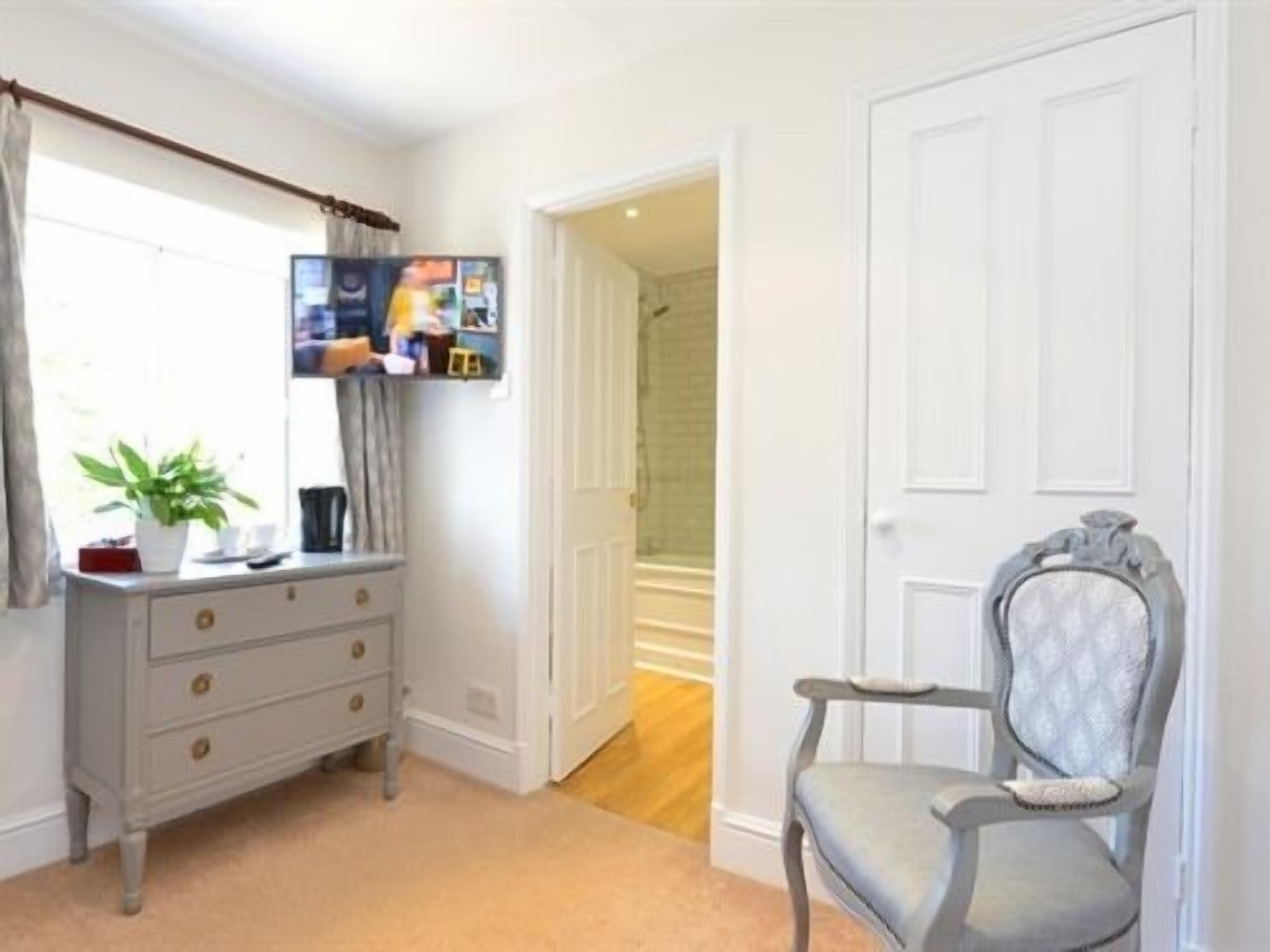 A room with a dresser, a chair, a television mounted on the wall, and a door leading to another room.