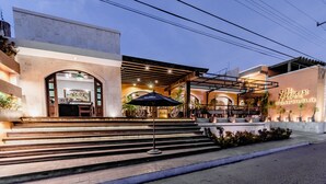 A hotel entrance with a bar area, outdoor seating, and a staircase leading to the entrance.
