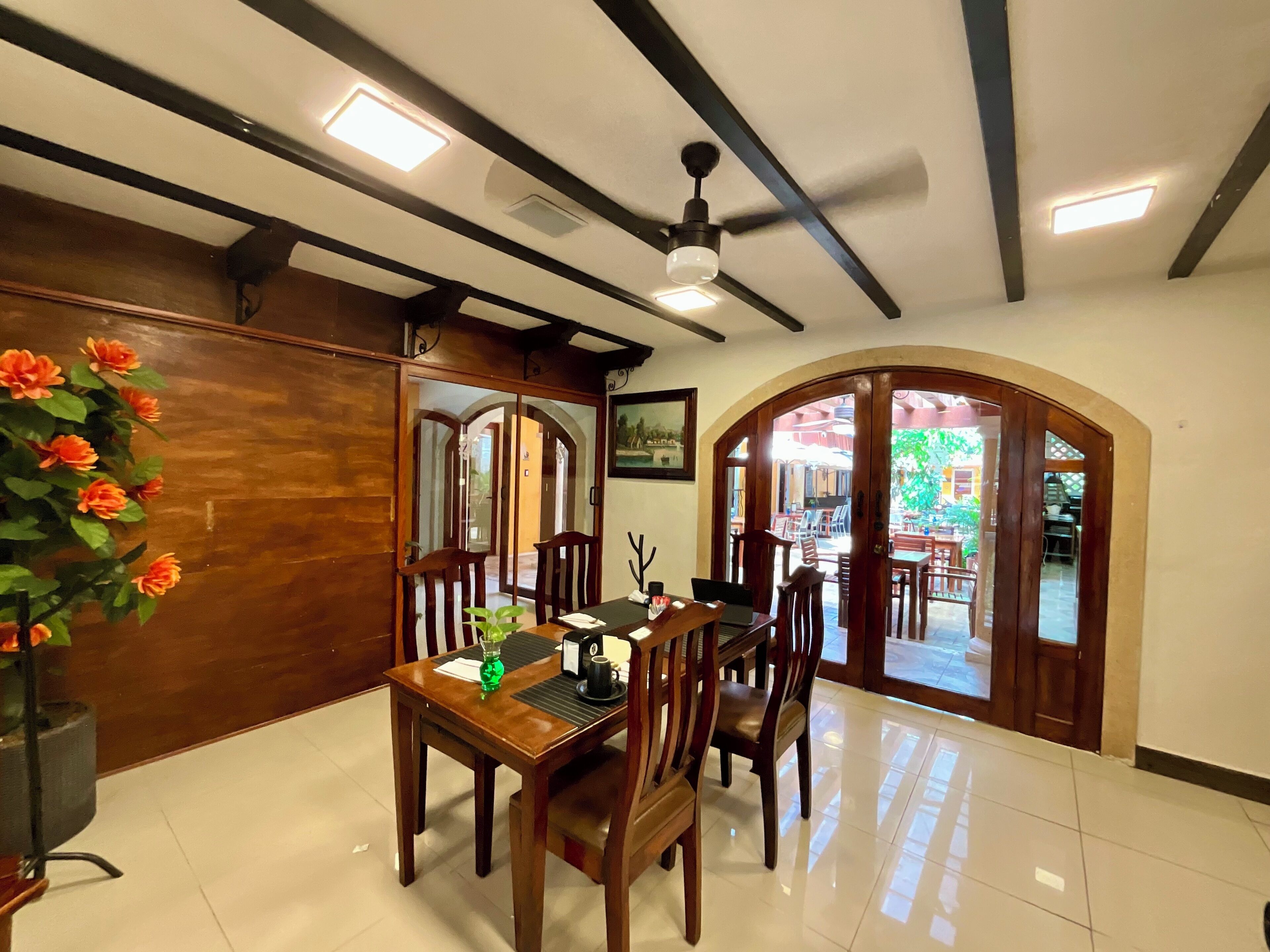 Un comedor con una mesa y sillas de madera, un ventilador de techo y vistas a una zona de estar exterior por un arco.