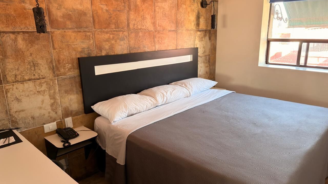 A neatly made bed with white linens in a room with a tiled wall and a small bedside table with a phone.
