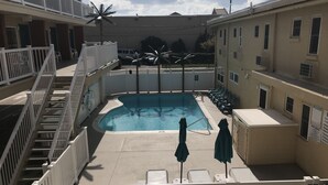 A rooftop pool area with a clear view of the sky, a palm tree, and a white fence. - Seahorse Inn (Wildwood)