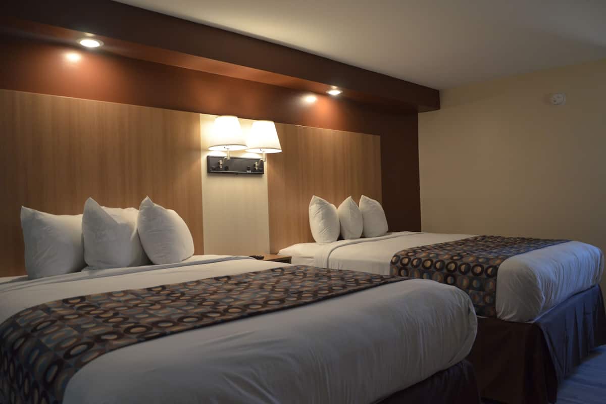 A hotel room with two beds, each with white linens and pillows, a wooden headboard, and a wall-mounted lamp.