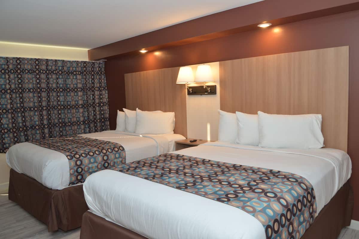 A hotel room with two beds, a patterned curtain, a wall-mounted lamp, and a wooden headboard.