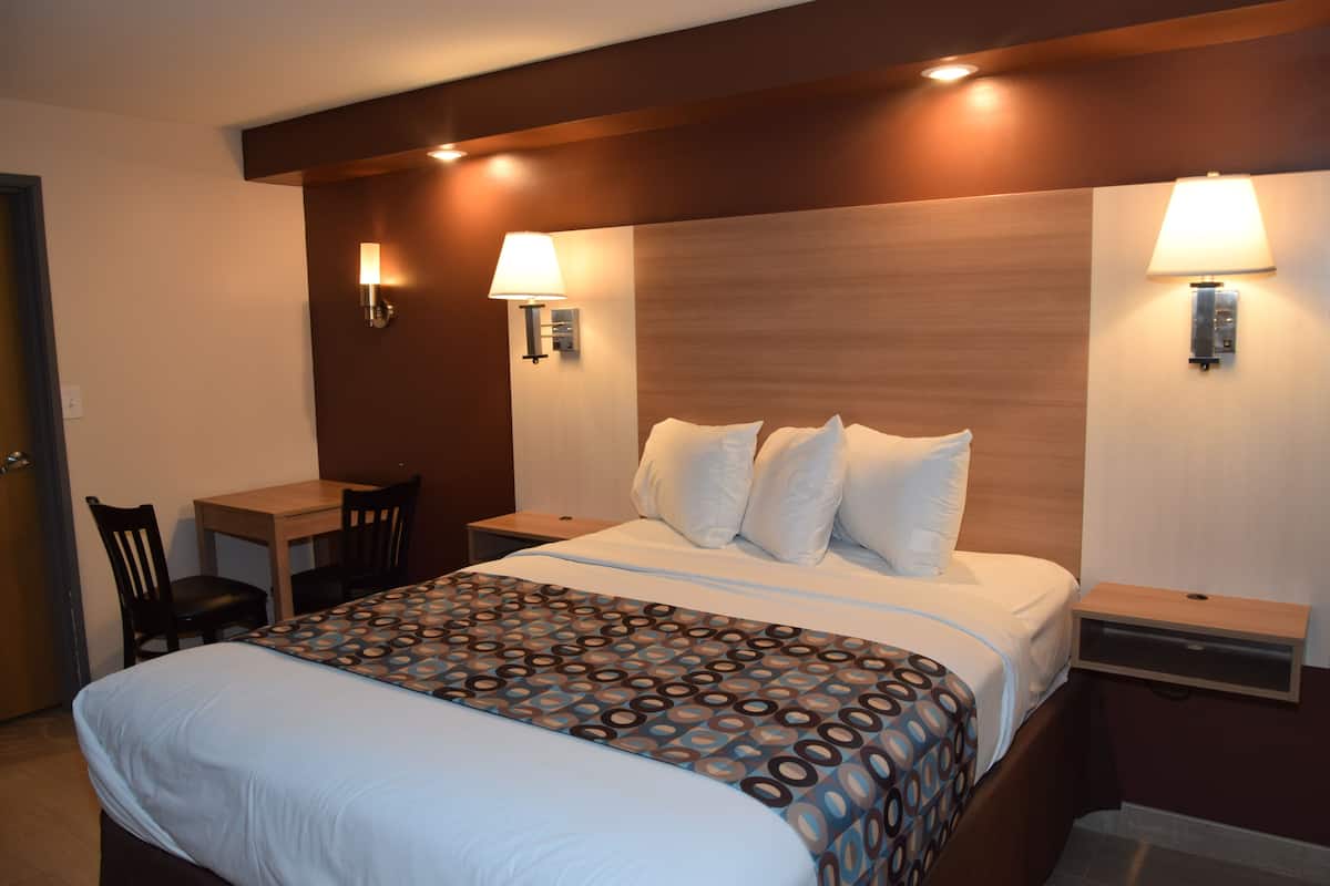 A hotel room with a large bed, two bedside tables, a desk with a chair, and two wall-mounted lamps.