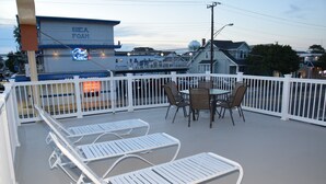 A rooftop deck with white lounge chairs, a table, and chairs. A neon sign for 'Sea Foam' is visible in the background. - Seahorse Inn (Wildwood)