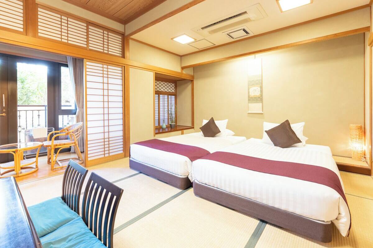A traditional Japanese-style hotel room with tatami flooring, a futon bed, a low table with chairs, and a sliding shoji screen.