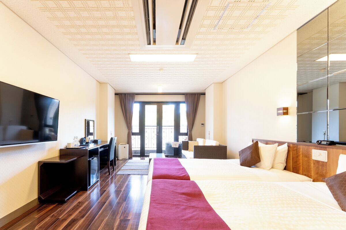 A hotel room with a bed, a desk, a television, and a large window.