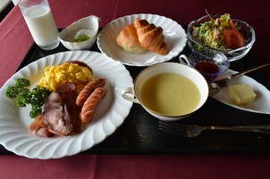 Una bandeja con alimentos para el desayuno, incluyendo huevos, salchichas, croissants, sopa y una ensalada.