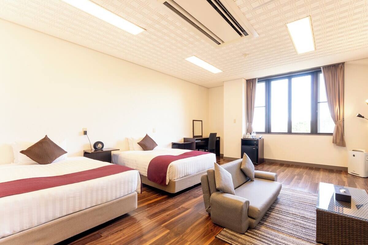 A hotel room with two beds, a sofa, a desk, and a large window.