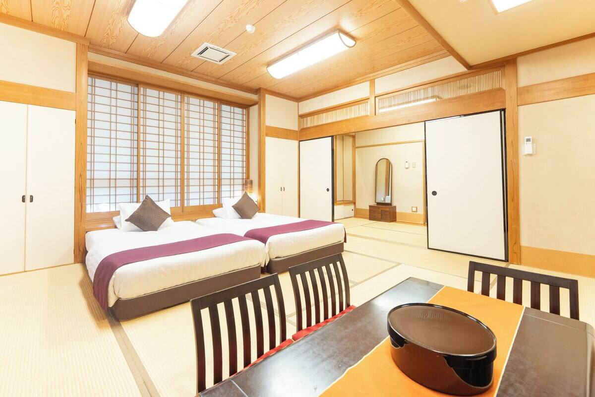 A traditional Japanese-style room with tatami flooring, a futon bed, a wooden table with a coffee pot, and sliding doors.