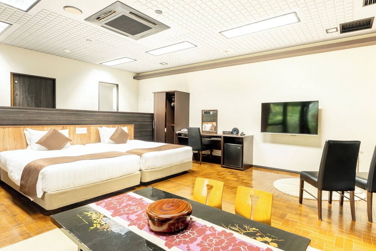 A hotel room with a double bed, a desk with a chair, a television, and a small seating area with a table and chairs.