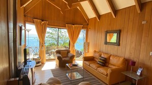 A cozy room with a wooden interior, a leather sofa, a glass coffee table, and a view of the outdoors.