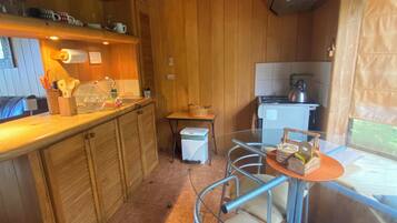 A kitchen with wooden cabinets, a dining area with metal chairs, a small table, and a kettle on the stove.