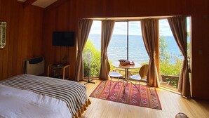 A bedroom with a large bed, a TV, a desk, and a view of the sea.