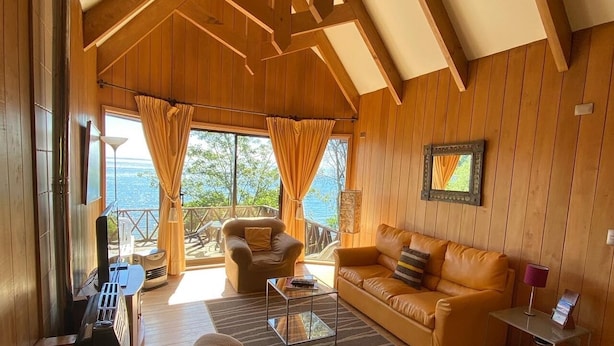 A cozy cabin interior with wooden walls, a sofa, a chair, and a table.