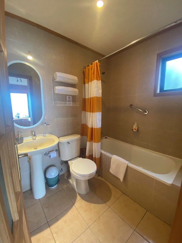 Un baño con lavamanos, inodoro y bañera. Hay una cortina de ducha y un perchero para toallas.