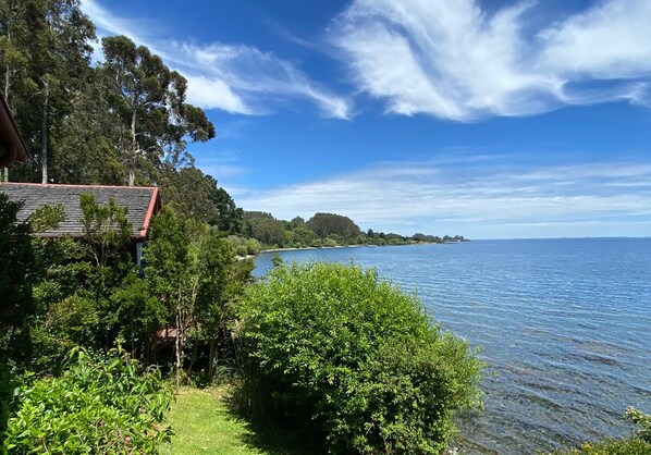 A coastal property with a house overlooking a calm sea, surrounded by lush greenery. - Cabañas Bahía Celeste (Puerto Varas)