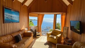 A cozy room with wooden paneling, a large window with curtains, a sofa, a chair, and a television.