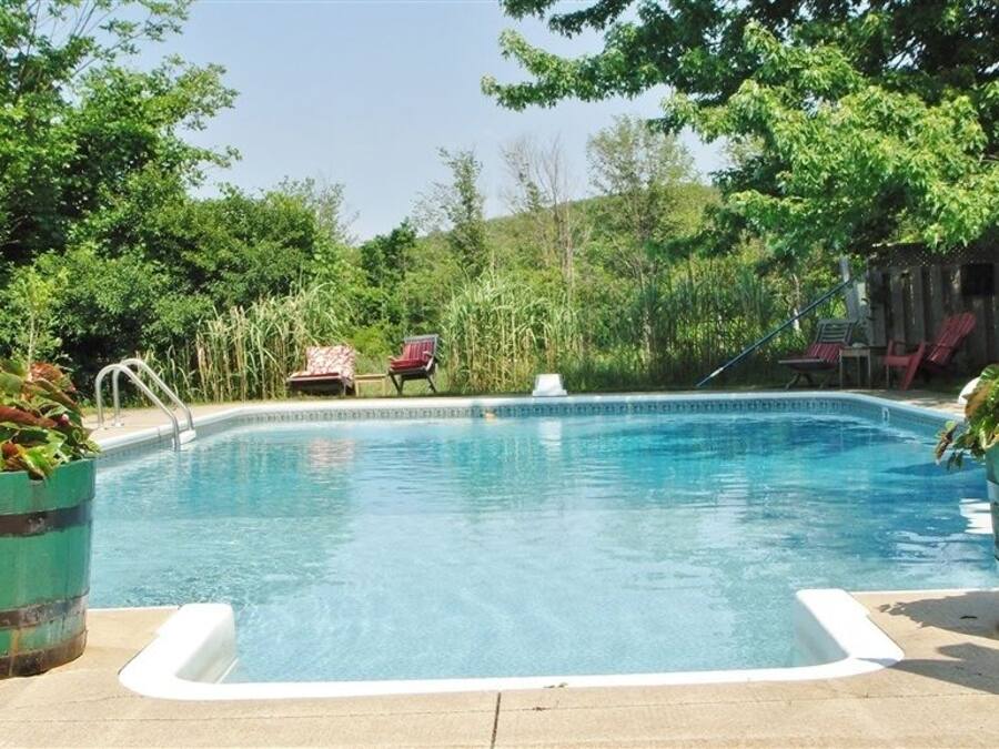 Une piscine avec un jacuzzi, entourée de verdure et dotée d’un espace salon extérieur.