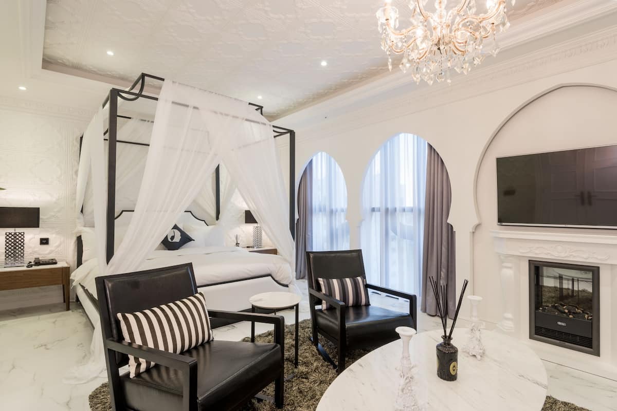 A luxurious bedroom with a four-poster bed, a sitting area with chairs, a marble table, and a fireplace.