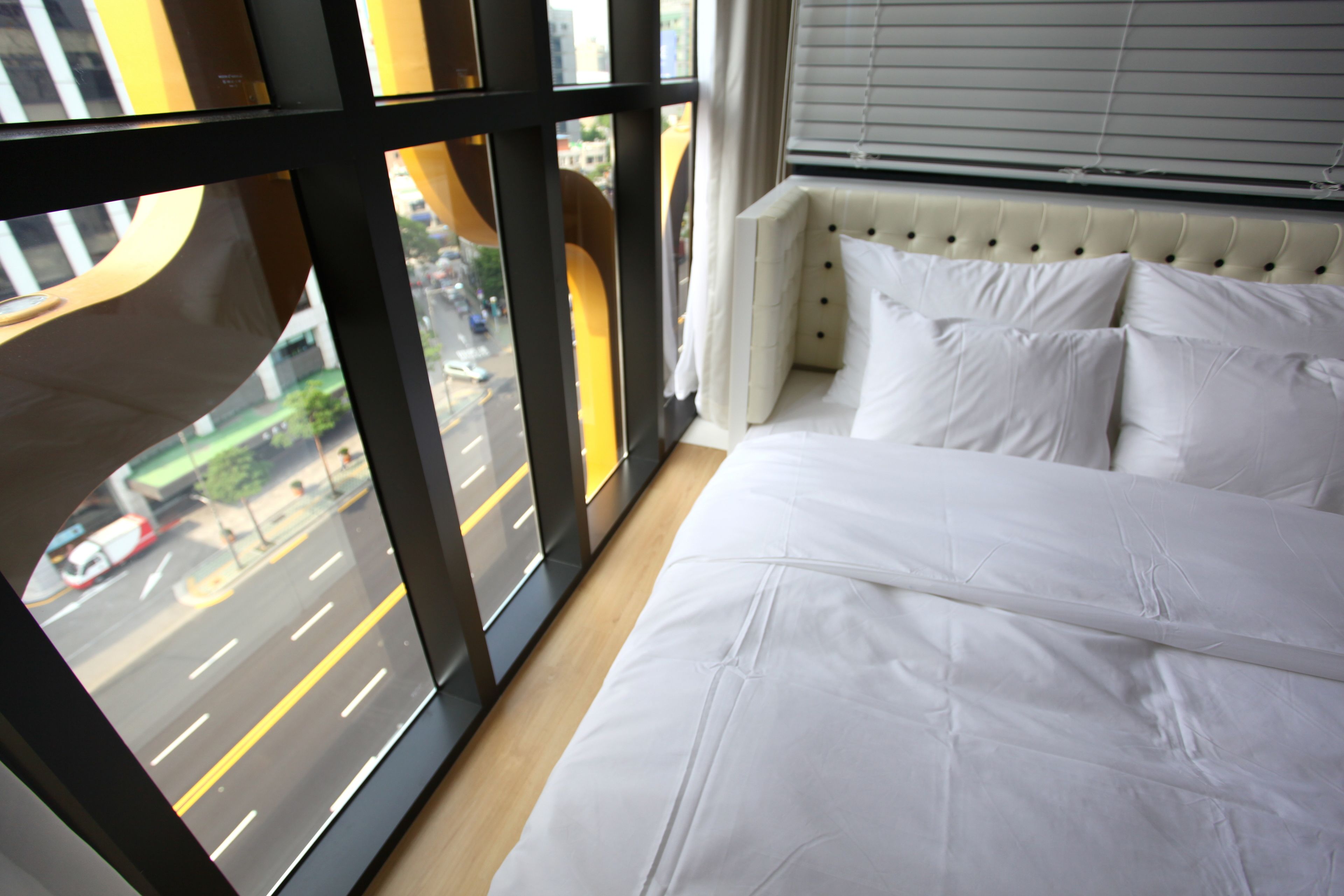 Habitación de hotel con un amplio ventanal que ofrece vistas a una calle concurrida.