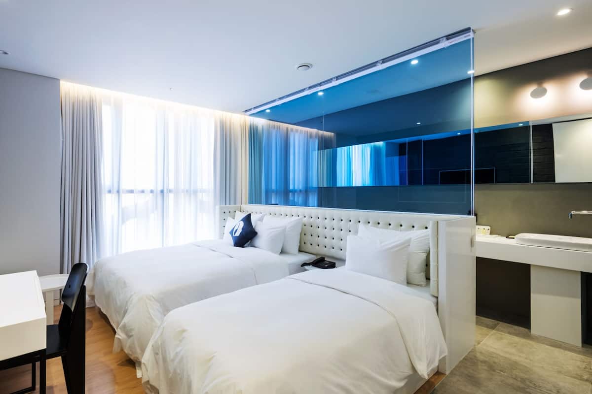 A modern hotel room with two beds, a desk, and a bathroom.