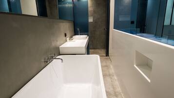 A modern bathroom with a large bathtub, two sinks, and a glass shower enclosure.