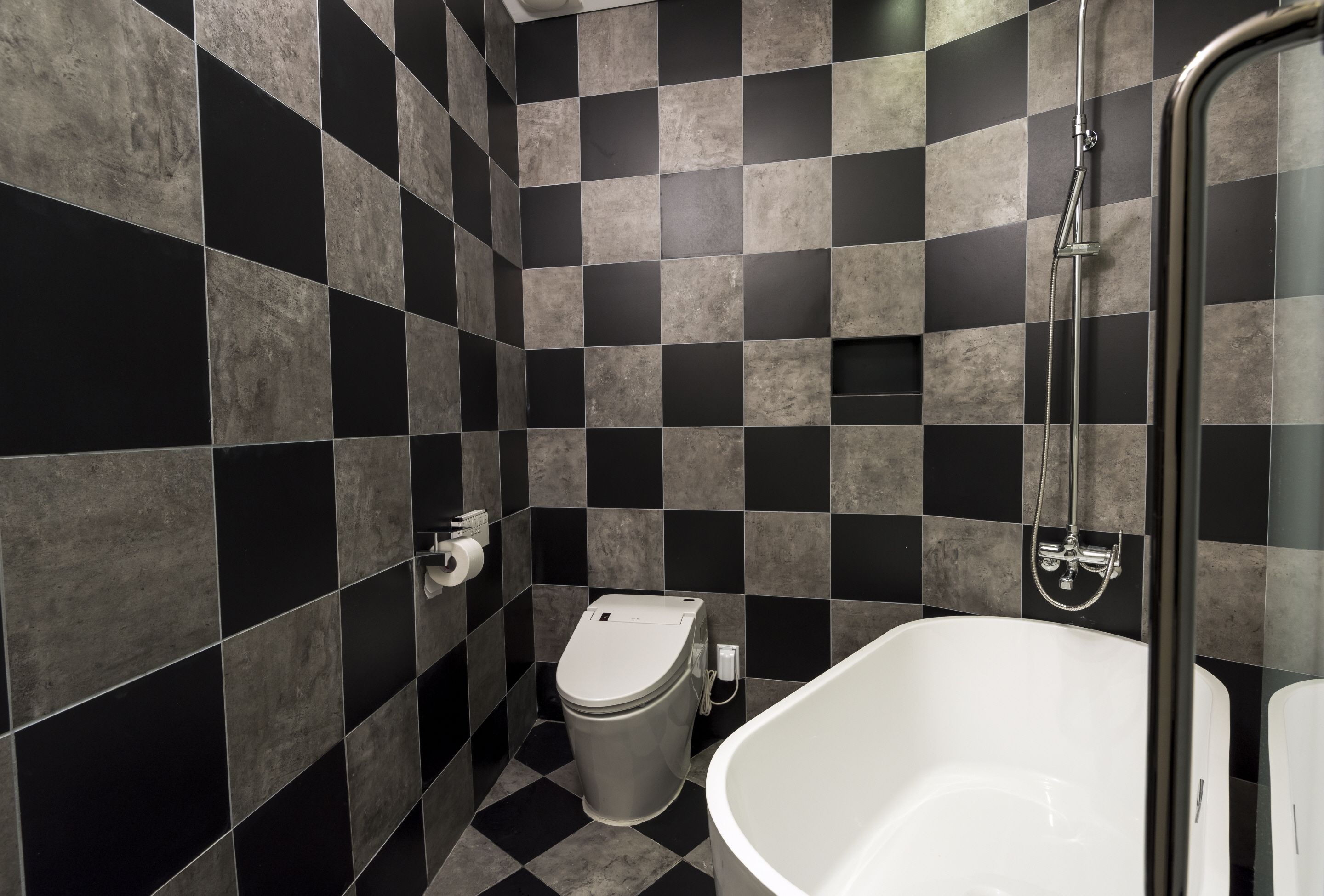 A bathroom with a checkered black and gray tile wall, a white toilet, and a white bathtub.