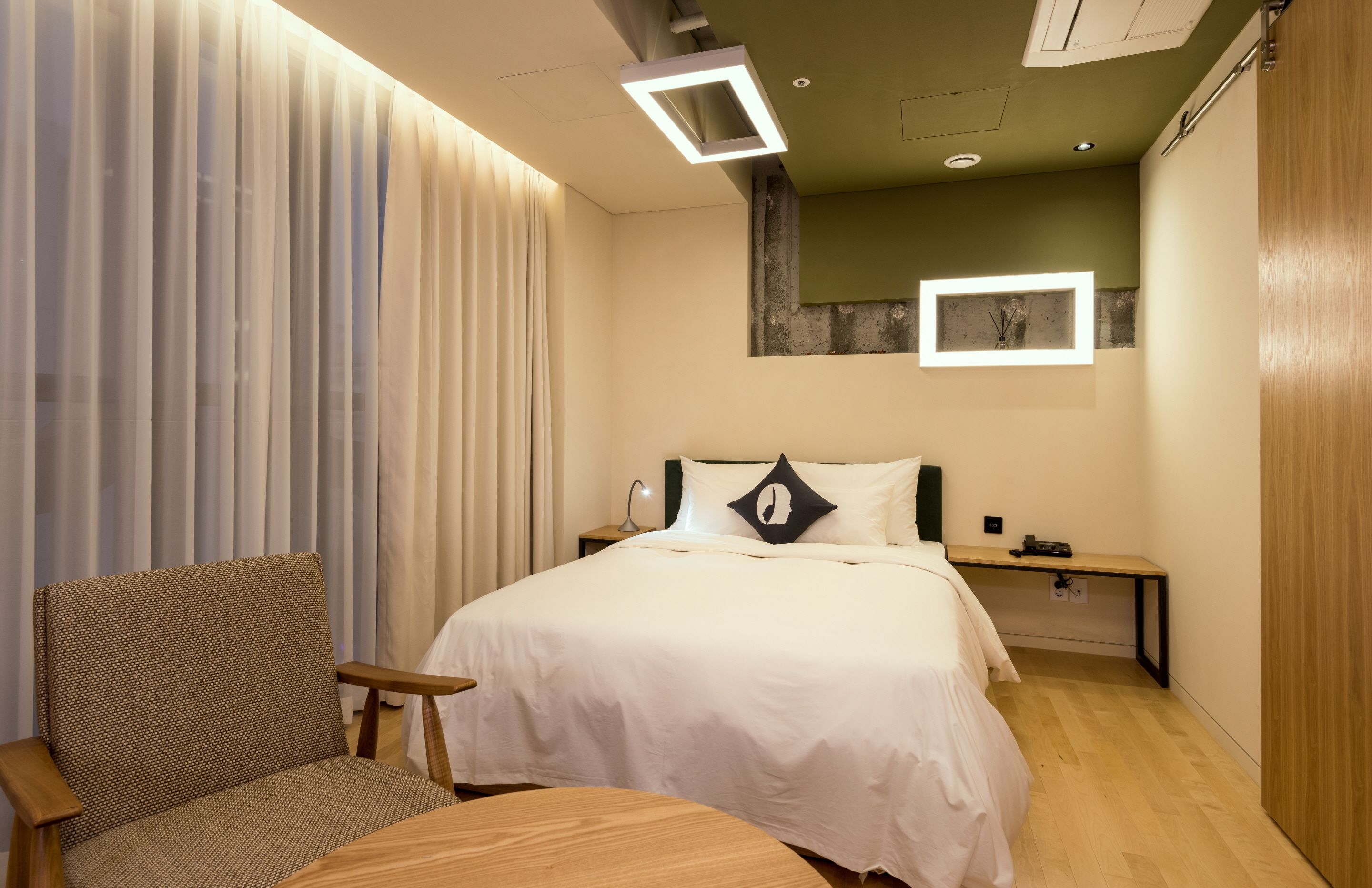 A modern hotel room with a large bed, a chair, a small table, and a nightstand.