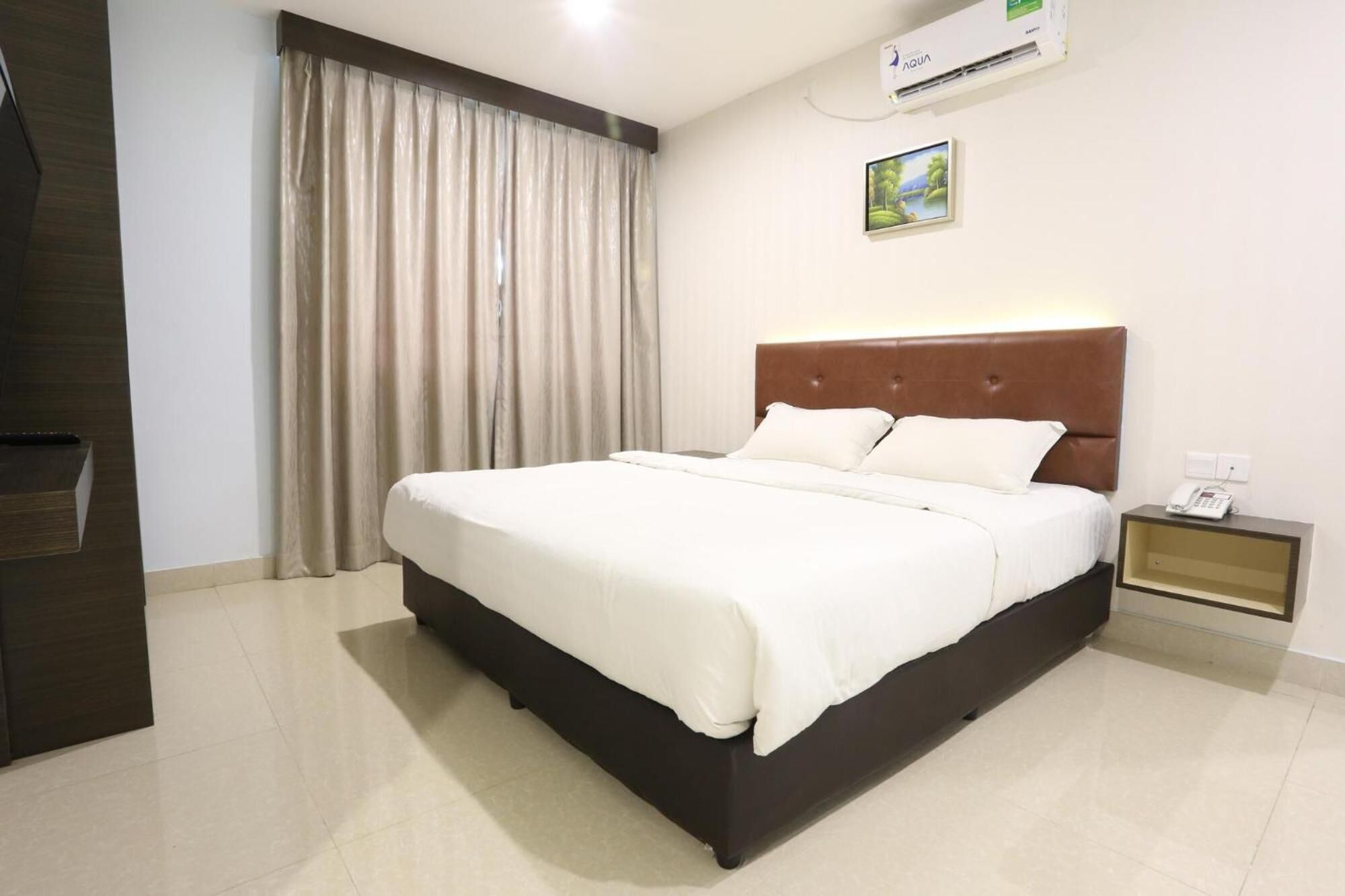 A hotel room with a large bed, a nightstand, an air conditioning unit, and a painting on the wall.