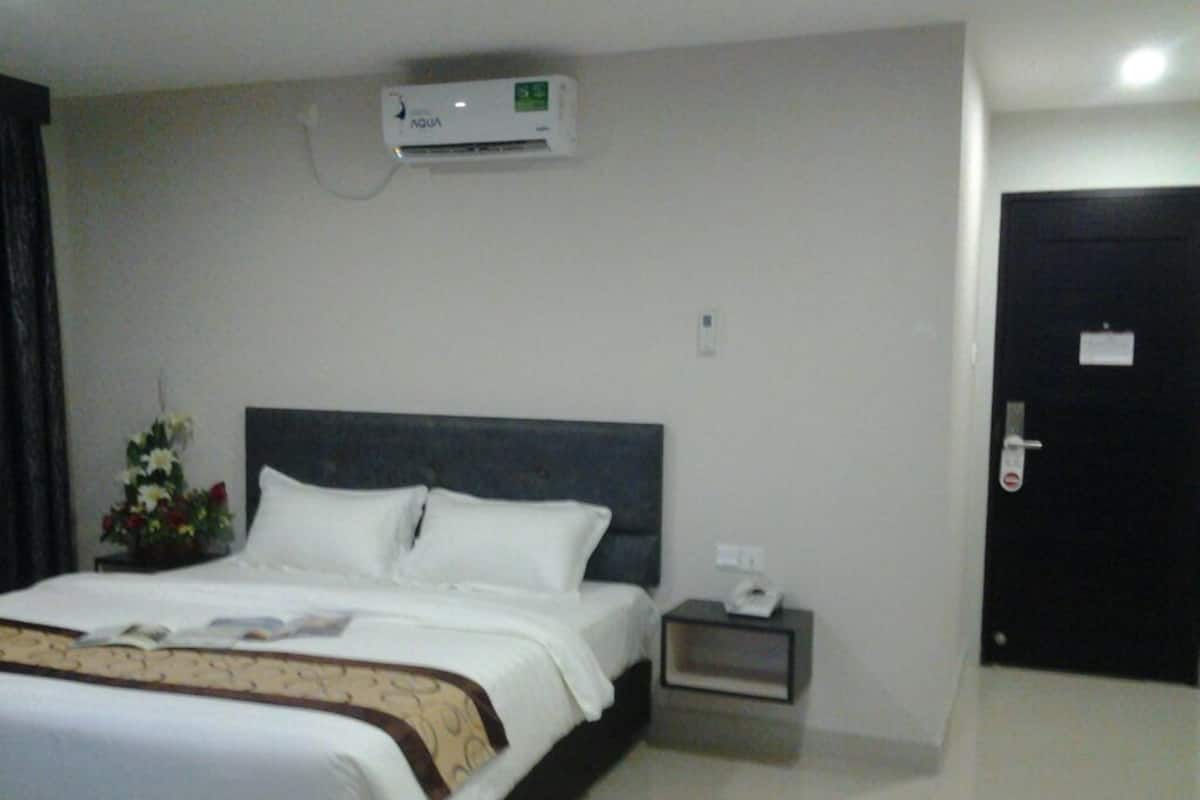 A hotel room with a bed, a bedside table with a phone, an air conditioning unit, and a door.