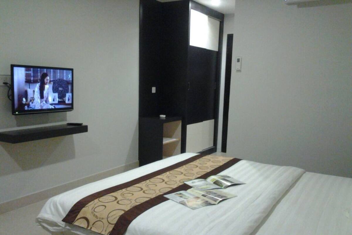 A hotel room with a bed, a television on the wall, and a door leading to a bathroom.