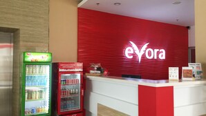 A reception area with a red 'eyvora' sign, a green and red Coca-Cola refrigerator, and a white counter. - Evora Hotel (Surabaya)
