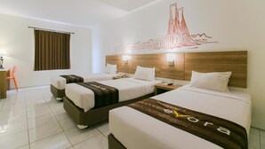 A hotel room with three beds, a wooden headboard, a wall mural, and a desk with a chair. - Evora Hotel (Surabaya)
