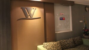 Una habitación con un sofá estampado, un estante montado en la pared con la letra 'V' y una ventana con un cartel de 'Free Wi-Fi'.