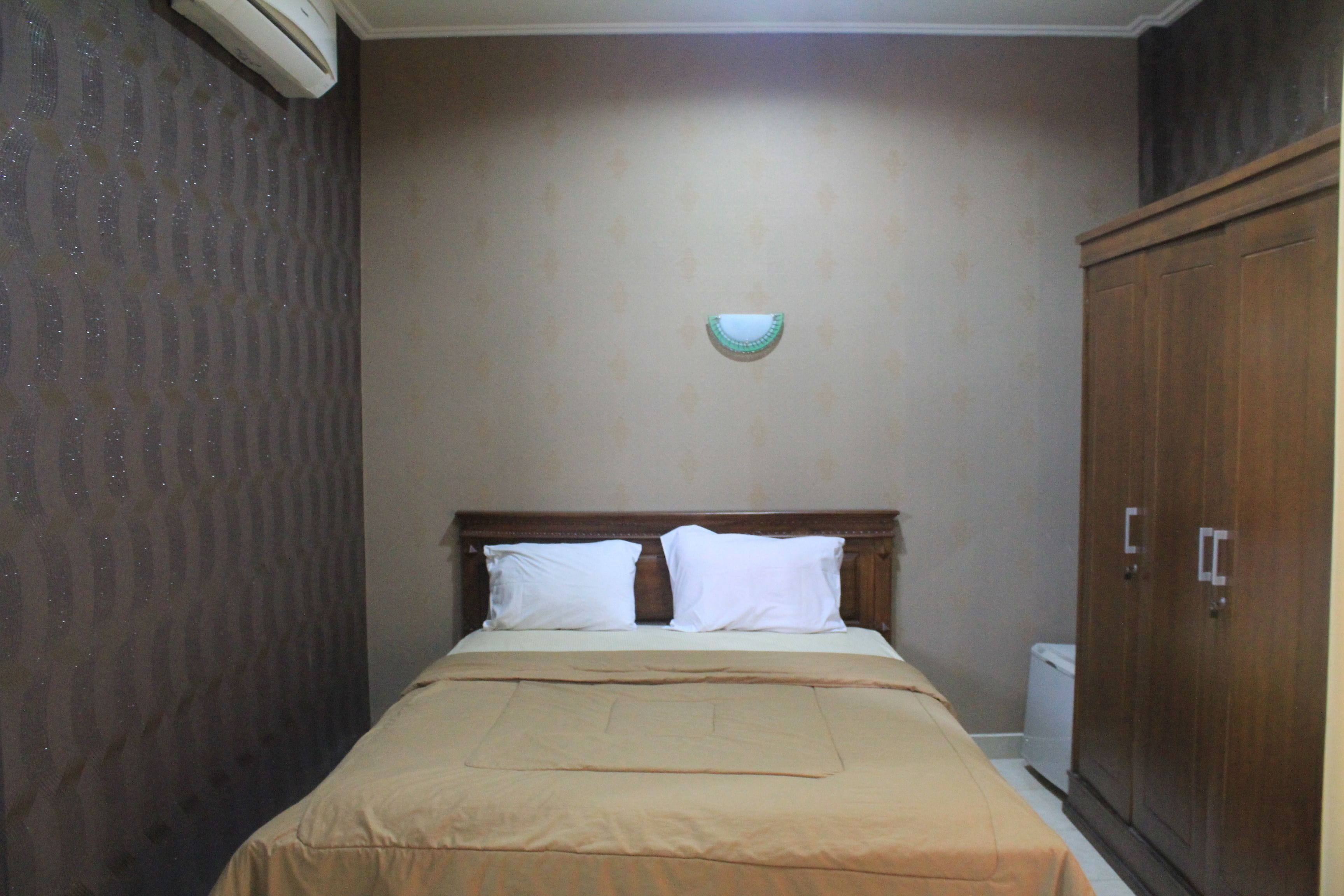 Quarto com cama, mesa de cabeceira, guarda-roupa e luminária na parede.