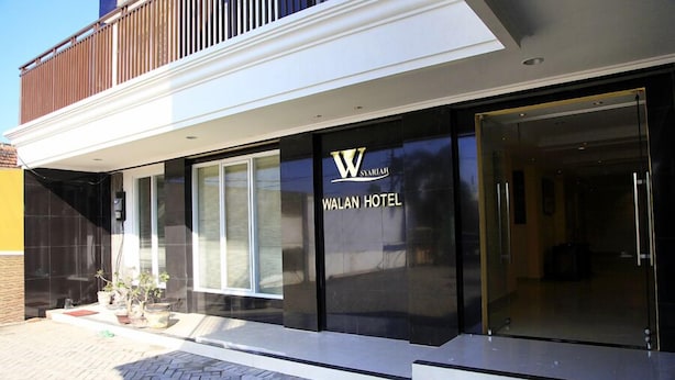 Una entrada de hotel moderna con fachada de vidrio, un logotipo destacado y una placa con el nombre.