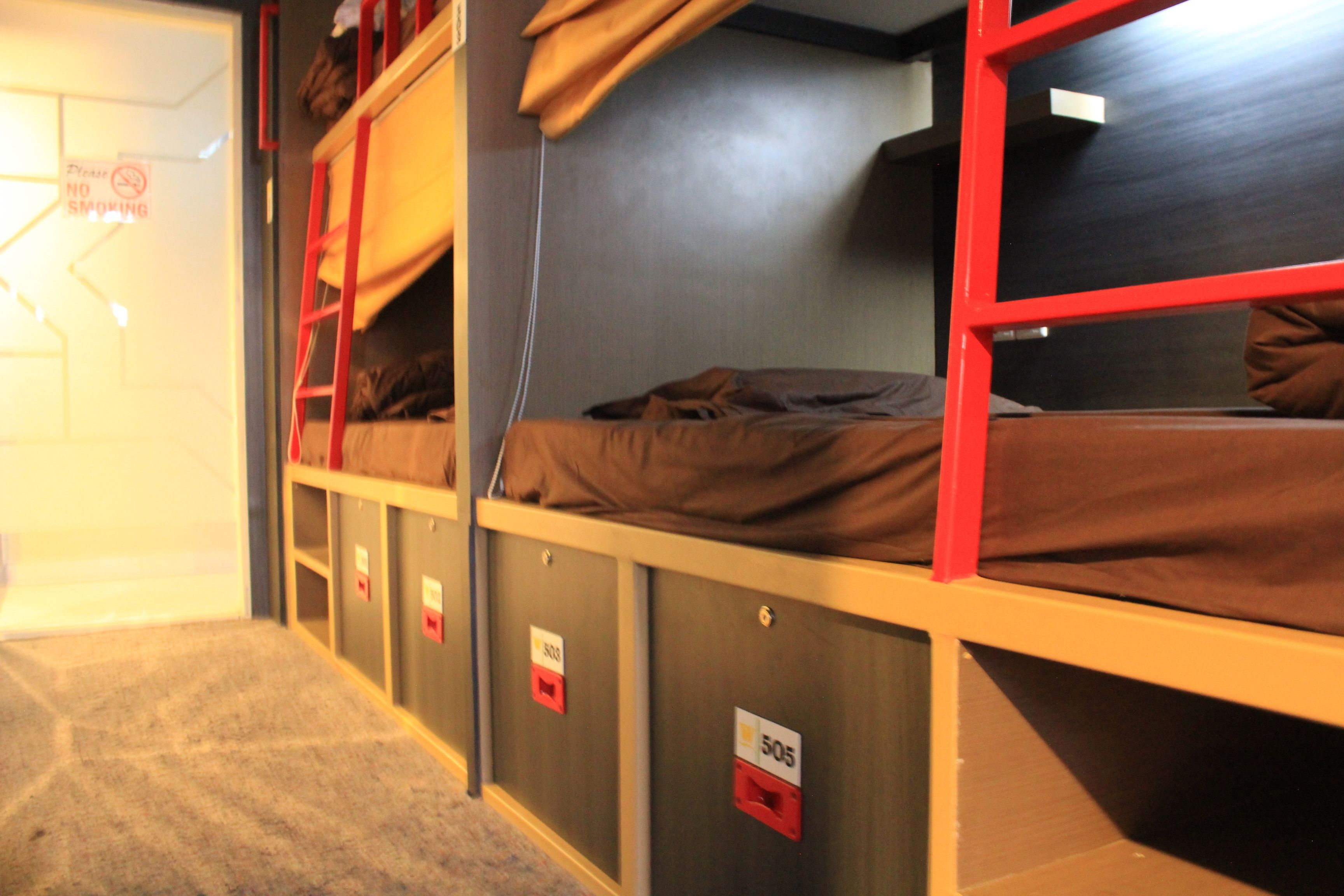 A bunk bed room with a "NO SMOKING" sign, a red ladder, and numbered lockers.