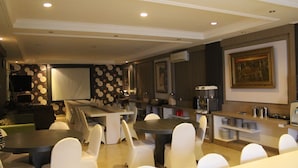 Un comedor moderno con mesas redondas y sillas blancas, una zona de cocina con electrodomésticos, y una pared decorada con un cuadro enmarcado.
