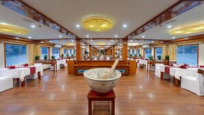 A dining area with tables set for service, a large decorative bowl in the center, and a view of the sea through large windows. - Huong Hai Sealife Cruise (Hong Gai)