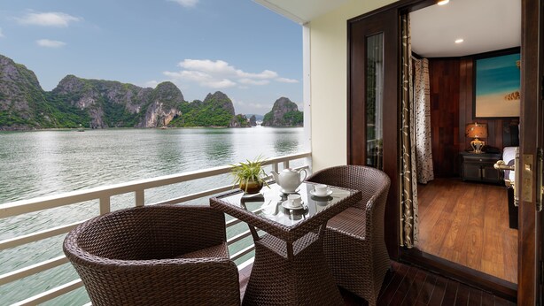 A balcony with wicker chairs, a table, and a view of a river and mountains. - Huong Hai Sealife Cruise (Hong Gai)